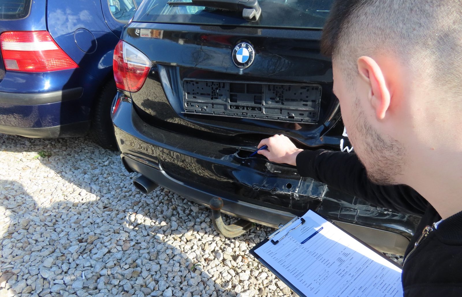 Kfz-Sachverständiger von Alterna nimmt den eingedrückten Heckstoßfänger eines Fahrzeugs auf und dokumentiert den Schaden auf dem Aufnahmebogen